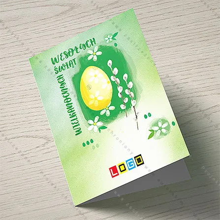 Jasnożółte jajo na ciemnozielonej plamie z bazią i białymi kwiatkami, po lewej pionowy napis wielkimi literami